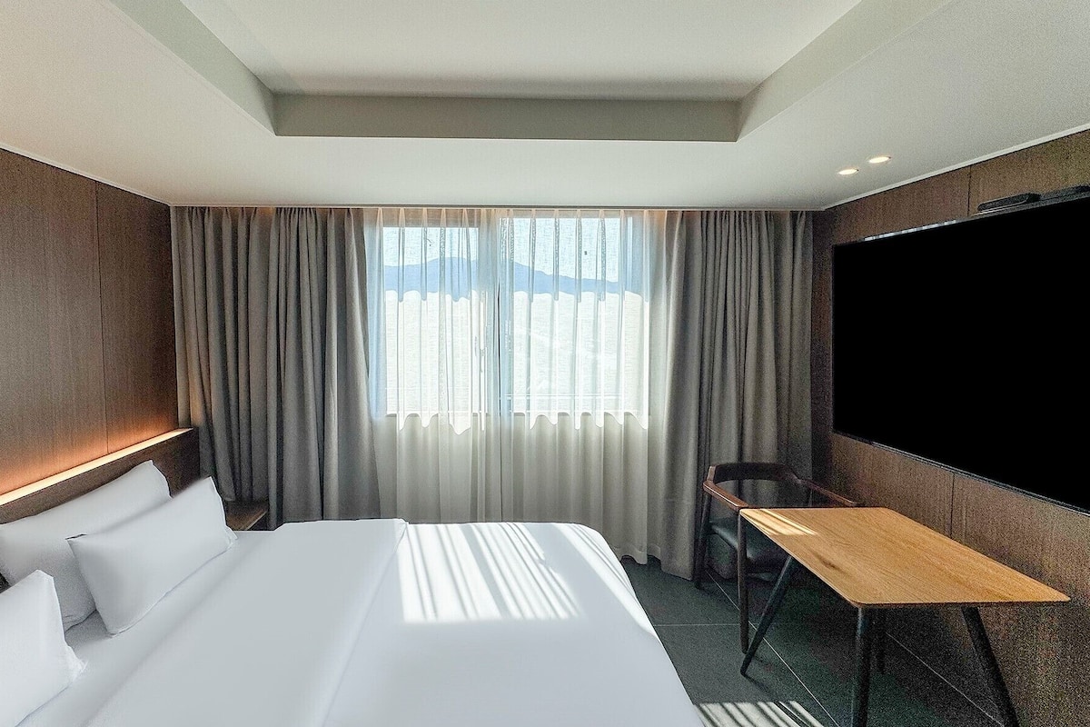 A hotel room with a large bed, a desk, and a TV.