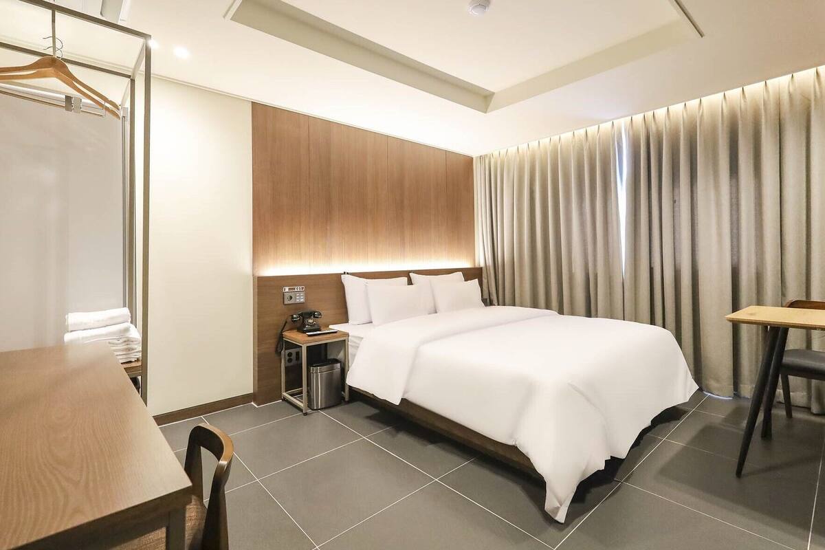 A modern hotel room with a neatly made bed, a desk, and a chair.