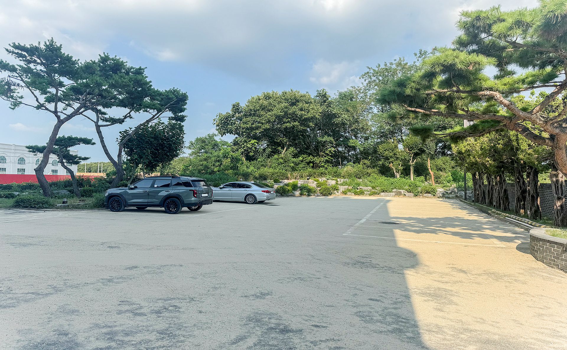 Ein Parkplatz mit zwei Autos, umgeben von Bäumen und einem Gebäude im Hintergrund.