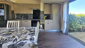 Una cocina moderna con electrodomésticos integrados, una zona de comedor con mantel estampado y un amplio ventanal corredero que da a un balcón.