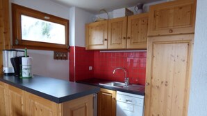 Une cuisine avec des meubles de rangement en bois, un plan de travail rouge recouvert de carreaux, un évier et un lave-vaisselle.