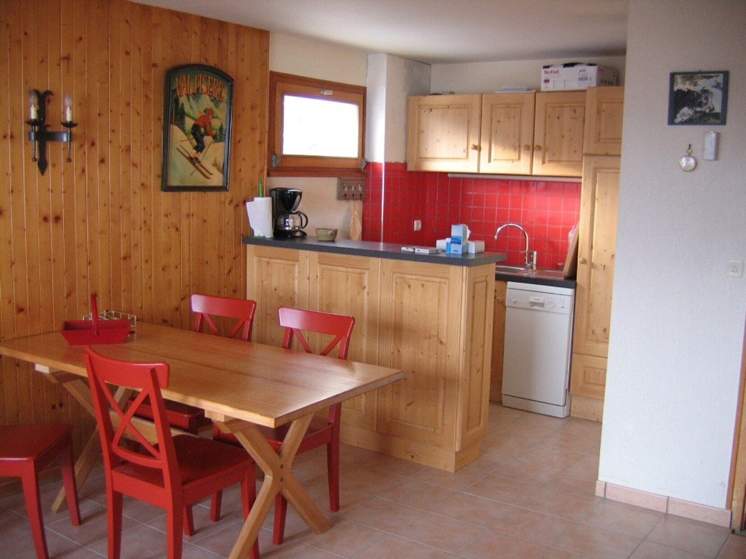 A kitchen with wooden cabinets, a dining table with red chairs, a coffee maker, and a dishwasher.