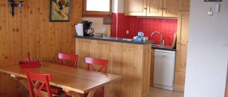 A kitchen with wooden cabinets, a dining table with red chairs, a coffee maker, and a dishwasher.