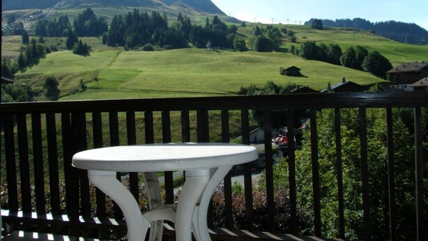 Un balcon avec une table blanche et une vue sur un paysage verdoyant, avec des collines et des arbres.