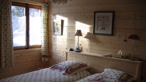 Une chambre avec deux lits, une fenêtre avec des rideaux, une table de chevet avec une lampe et des tableaux encadrés au mur.