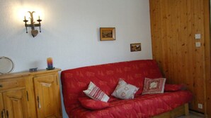 Une pièce chaleureuse avec un canapé rouge à motifs, un meuble en bois et un luminaire fixé au mur.