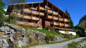 A multi-story building with balconies, situated on a hillside with a paved path leading to it.