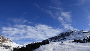 A snowy mountain landscape with clear skies and a few scattered clouds.