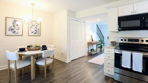 A modern kitchen with white cabinetry, a black microwave, and a stainless steel oven. There is a dining table with chairs and a chandelier above. - "The Spartan Reb" - The Perfect Oxford Getaway! (Oxford)
