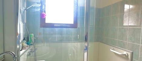 Un baño con ducha envuelta en vidrio, un lavamanos y un espejo.