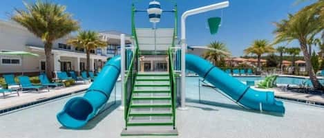 A pool area with two blue slides, a green staircase, and lounge chairs.