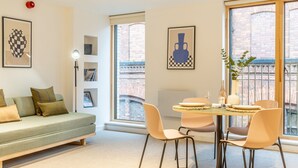Un salon moderne avec un canapé, une table à manger et des chaises, ainsi que de grandes fenêtres donnant sur un immeuble en briques.
