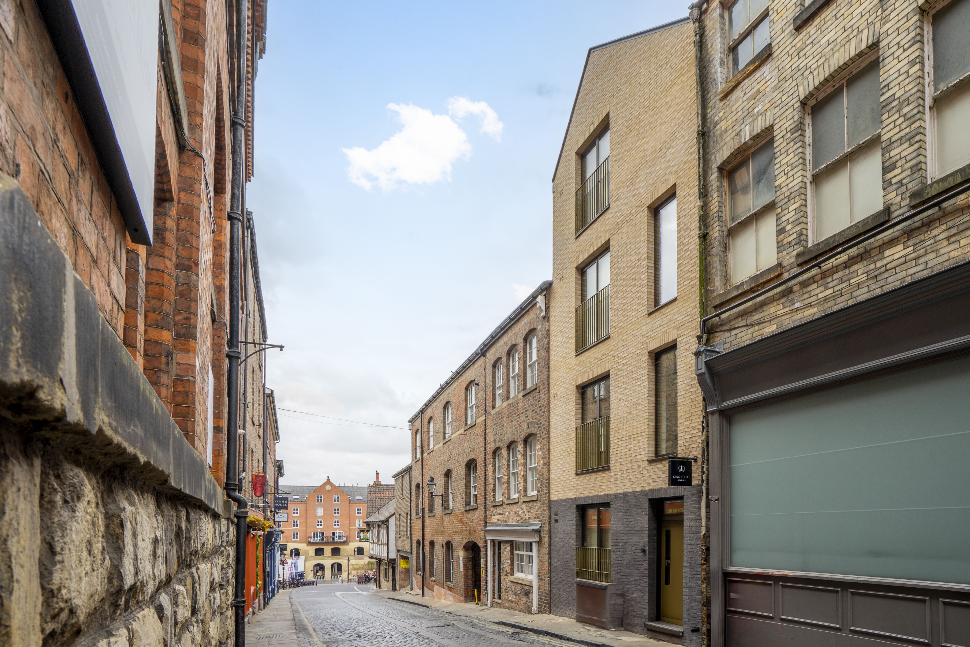 Une rue étroite bordée de bâtiments historiques, une chaussée pavée et un ciel dégagé.