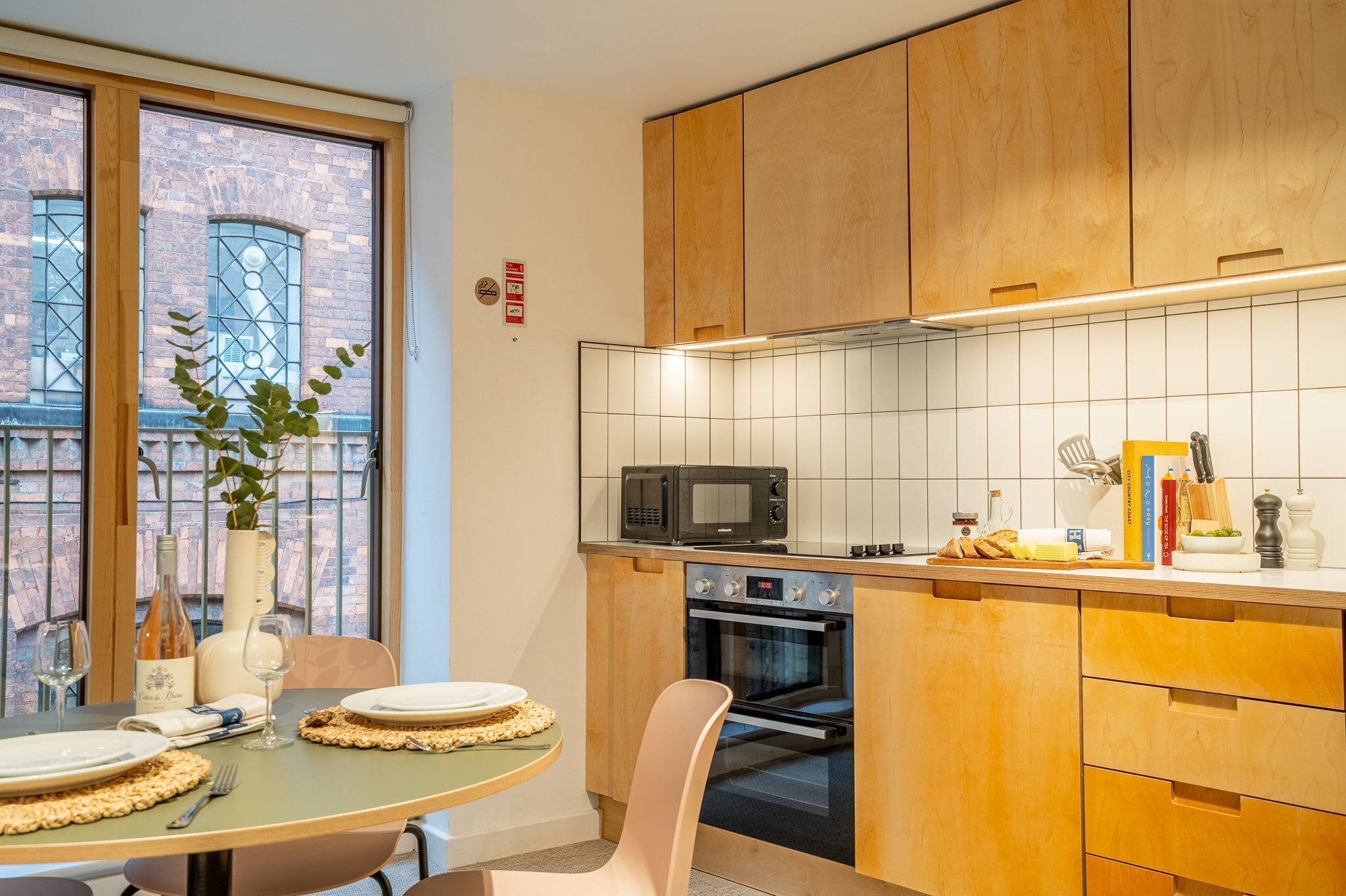 Cocina moderna con armarios de madera, microondas, horno y comedor con mesa puesta para dos.