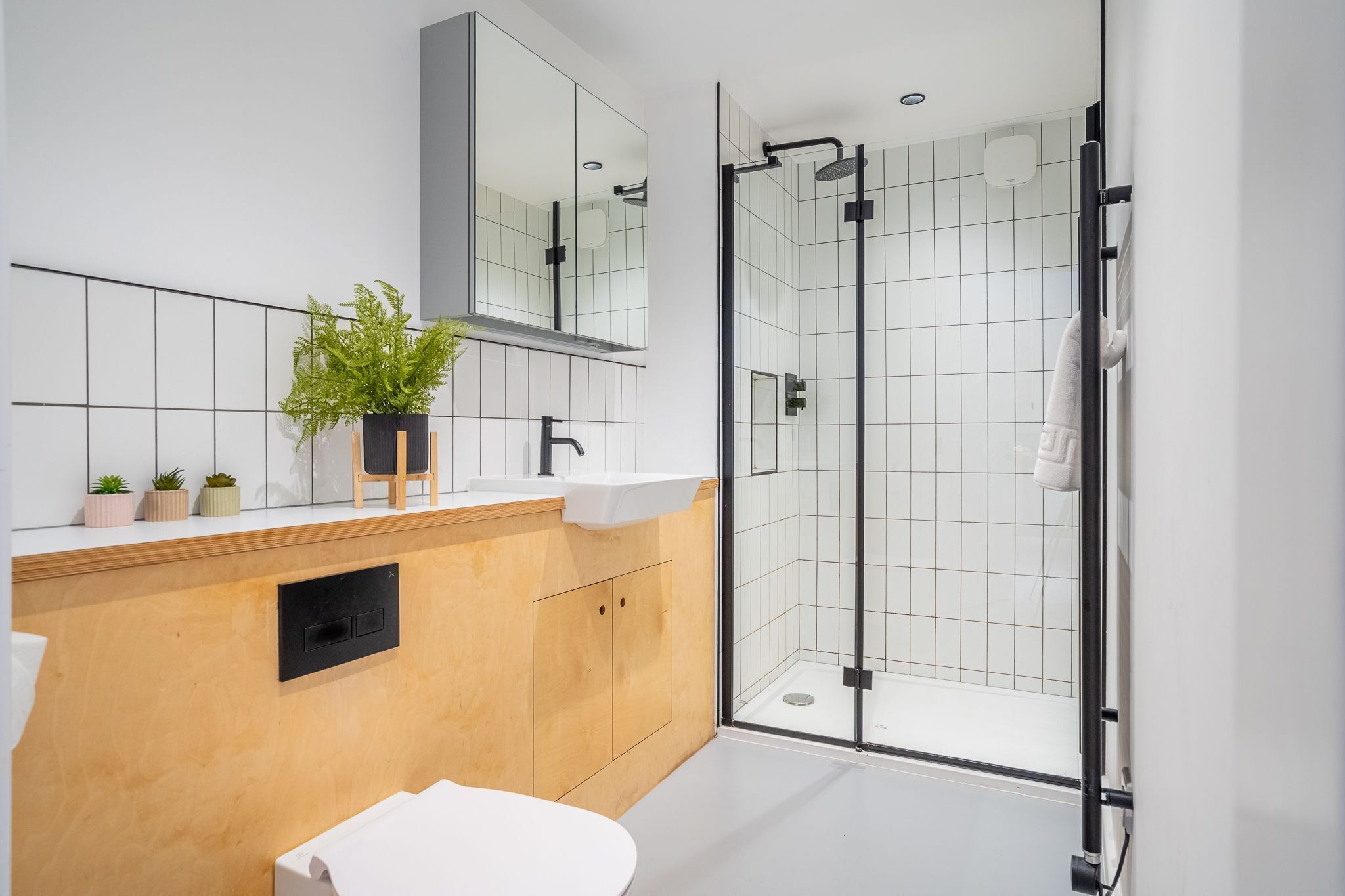 A modern bathroom with a wooden vanity, white sink, and a glass-enclosed shower.