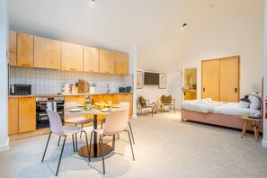 Um espaço compacto com cozinha americana, área de refeições e quarto com cama e mesa de cabeceira.