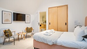 A hotel room with a bed, two chairs, a small table, a TV, and a wardrobe. - King Street Studios - King Henry IV (York)