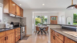 A modern kitchen with wooden cabinets, a dining area with a table and chairs, and a view of the outdoors through a glass door. - Modern 2BR in DT Renton, 3 AC, WS 95, Shop&Parks (Renton)