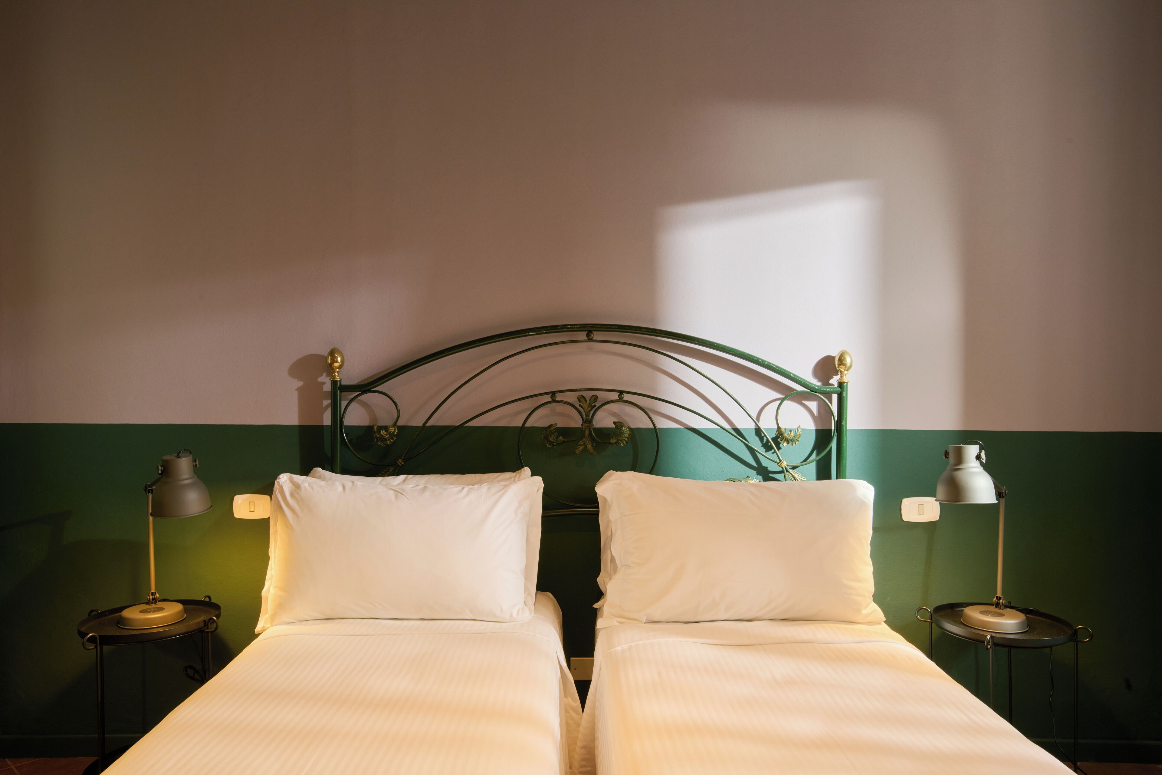 A double bed with two bedside tables, each with a lamp, in a room with a green and white wall.