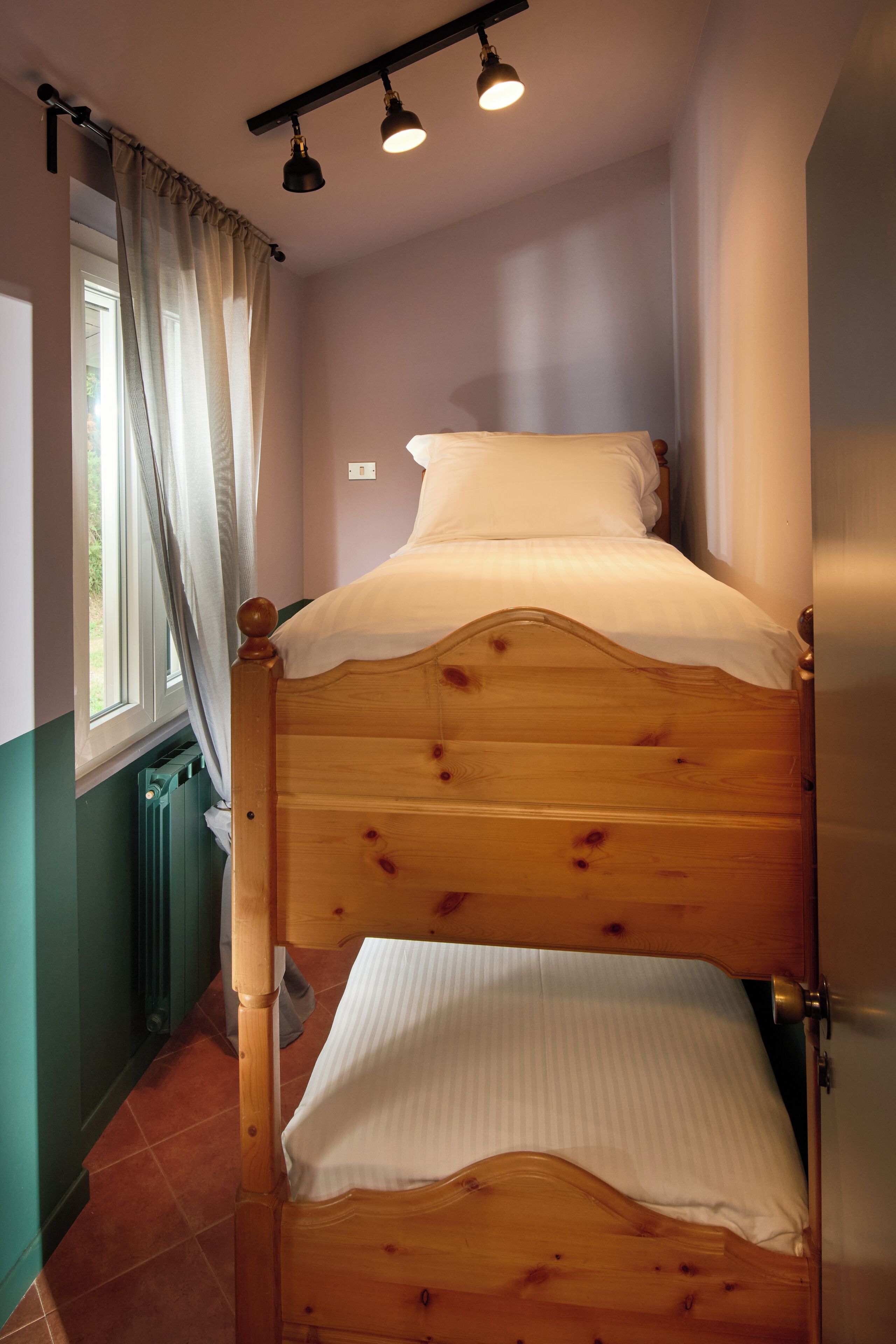 A bunk bed with a wooden headboard and a window with curtains.