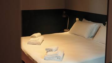 A neatly made bed with white linens and towels, a bedside lamp, and a dark headboard in a hotel room.