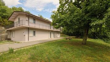 Een gebouw met twee verdiepingen, een balkon, een verharde oprit en een gazon met bomen.