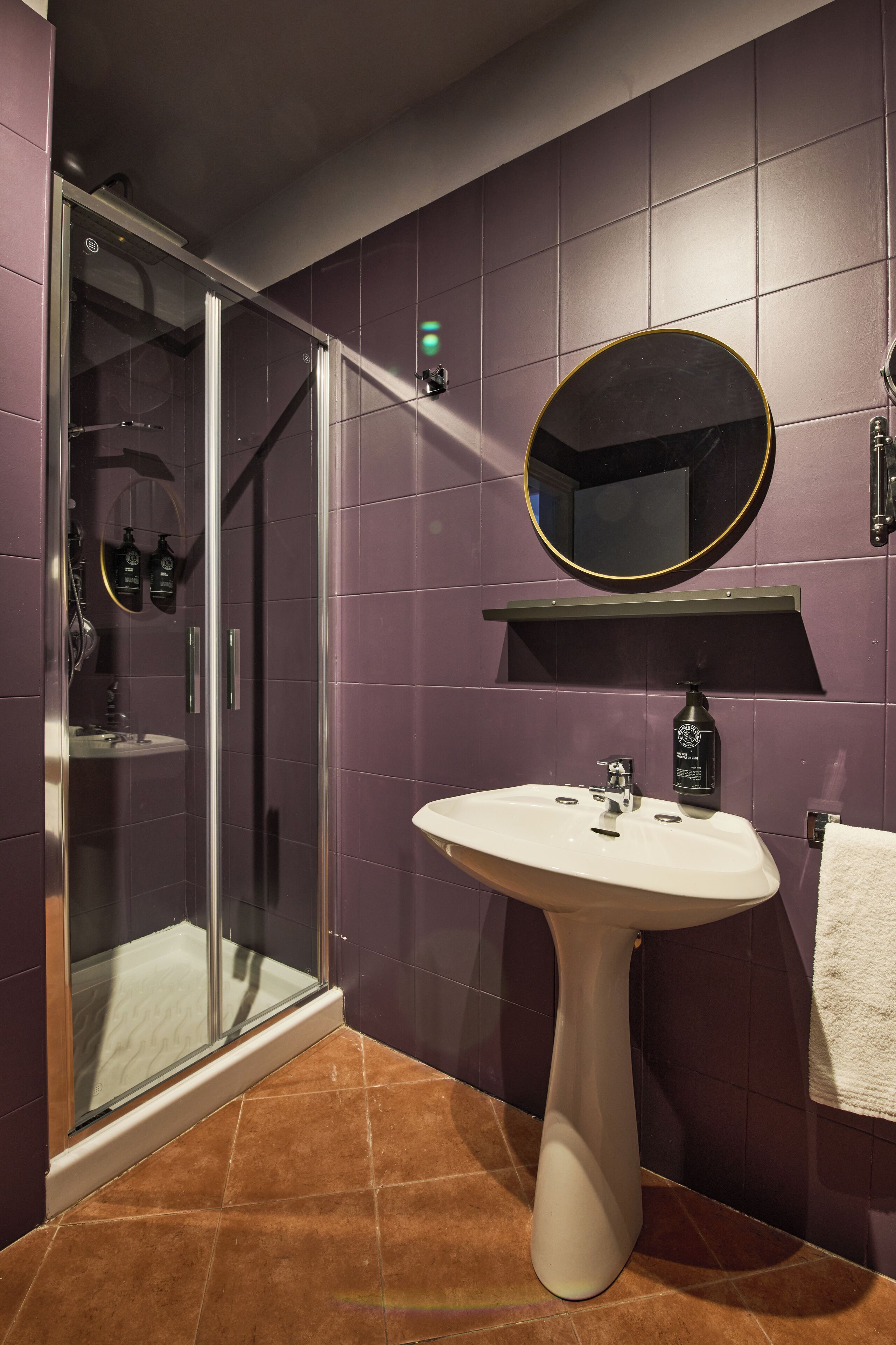 Ein Badezimmer mit einer Duschkabine, einem Standwaschbecken, einem Spiegel und violetten Fliesenwänden.