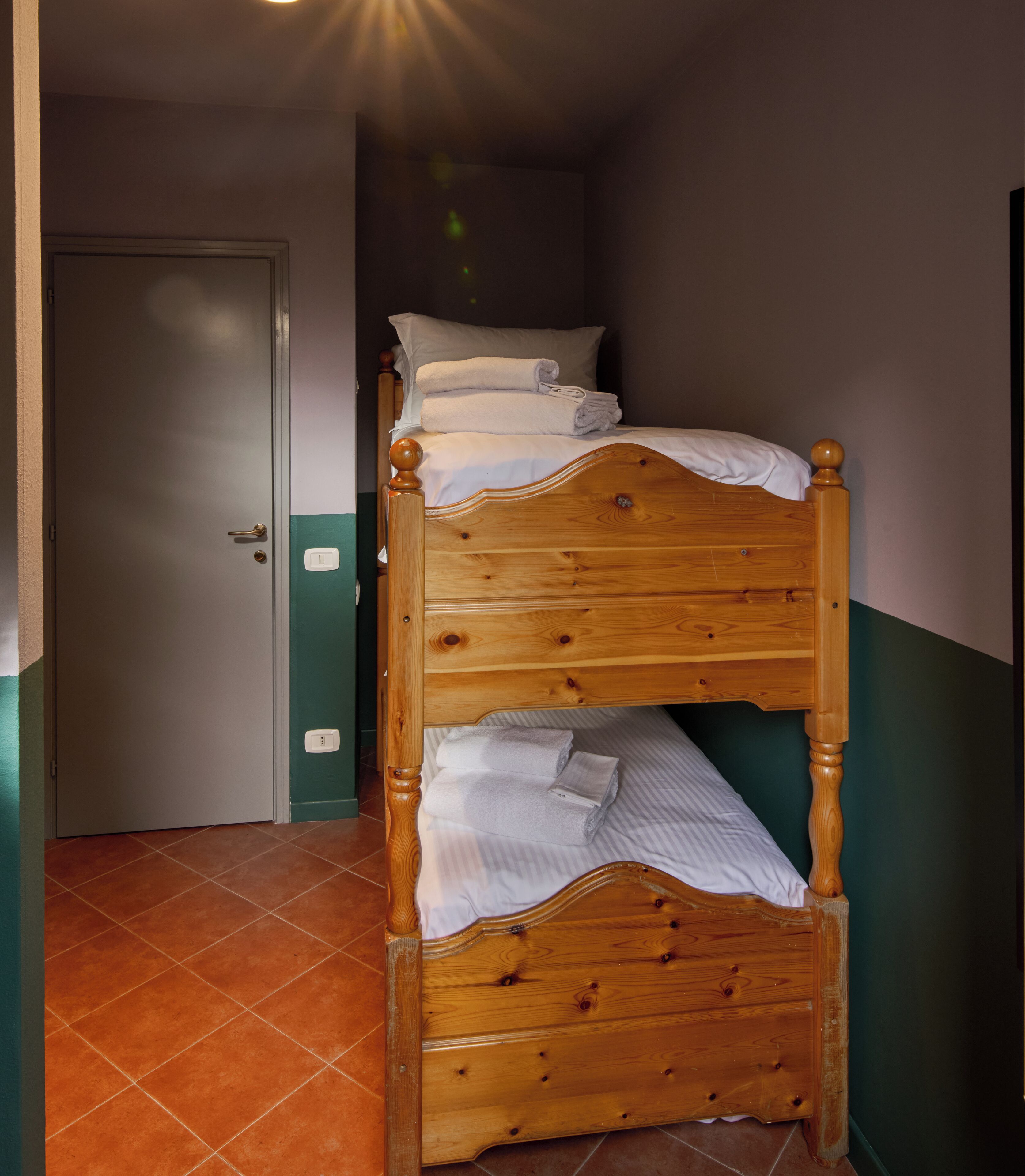 A wooden bunk bed with pillows and folded towels, a door, and a tiled floor.