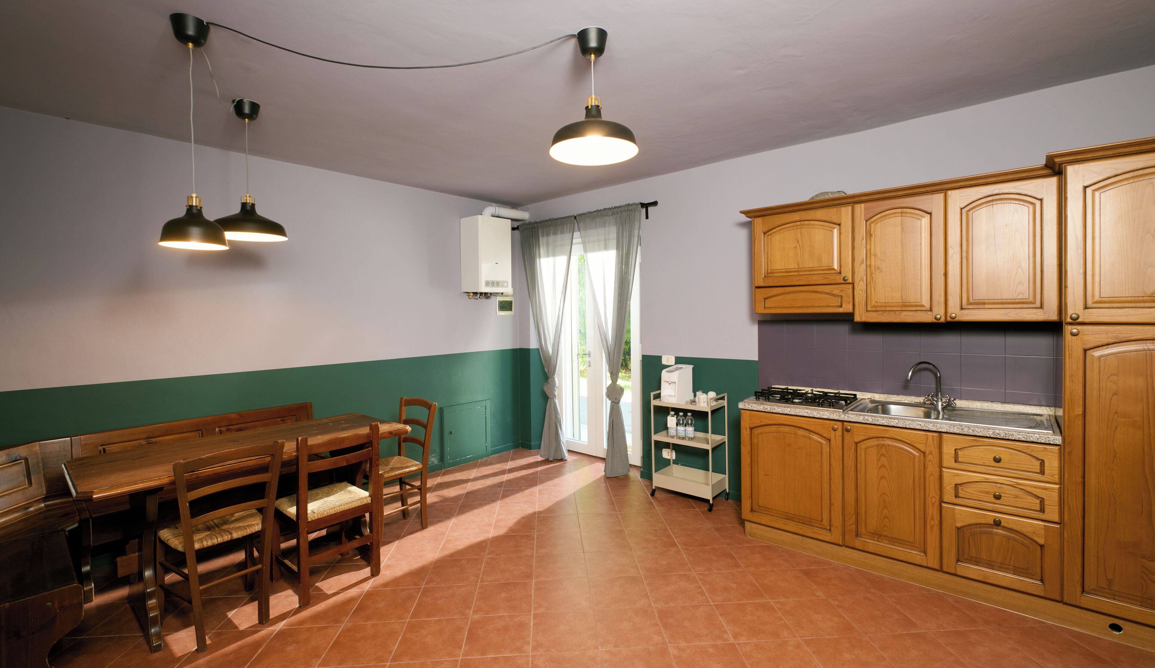 Une cuisine avec des meubles de rangement en bois, une table à manger avec des chaises et des luminaires suspendus.