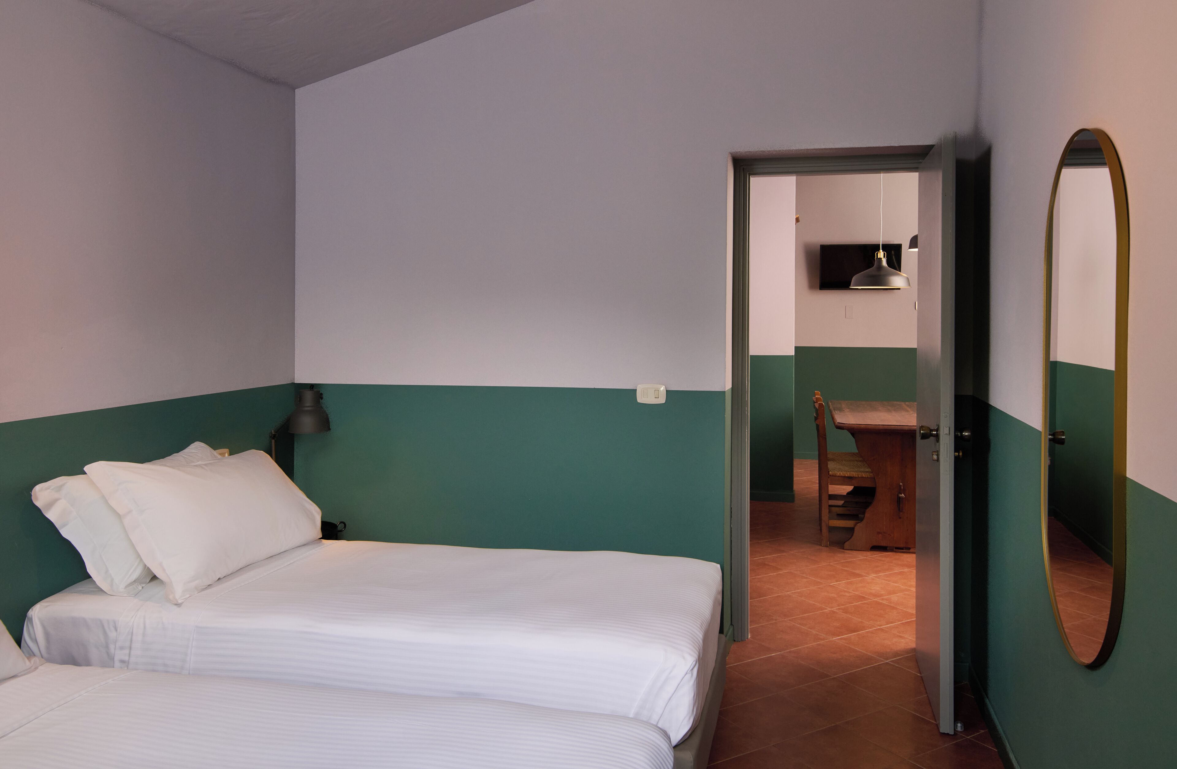 A bedroom with two beds, a desk, and a mirror.