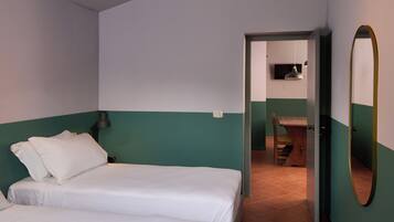 A bedroom with two beds, a desk, and a mirror.