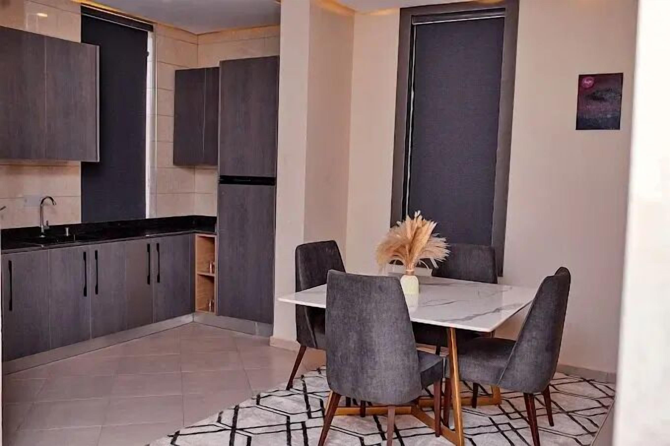 A modern kitchen with dark cabinets, a white countertop, and a dining area with a table and chairs.