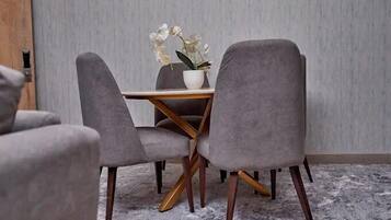 A dining area with a table and four grey upholstered chairs with wooden legs. A white vase with flowers is on the table.