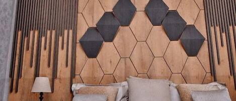 A modern bedroom with a wooden headboard, a bed with multiple pillows, a bedside table with a lamp, and a phone.