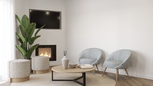 Een moderne woonkamer met een open haard, twee grijze fauteuils, een ronde salontafel en een grote plant.