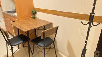Une petite cuisine équipée d’un évier et de placards, une table en bois avec deux chaises et une petite plante en pot.
