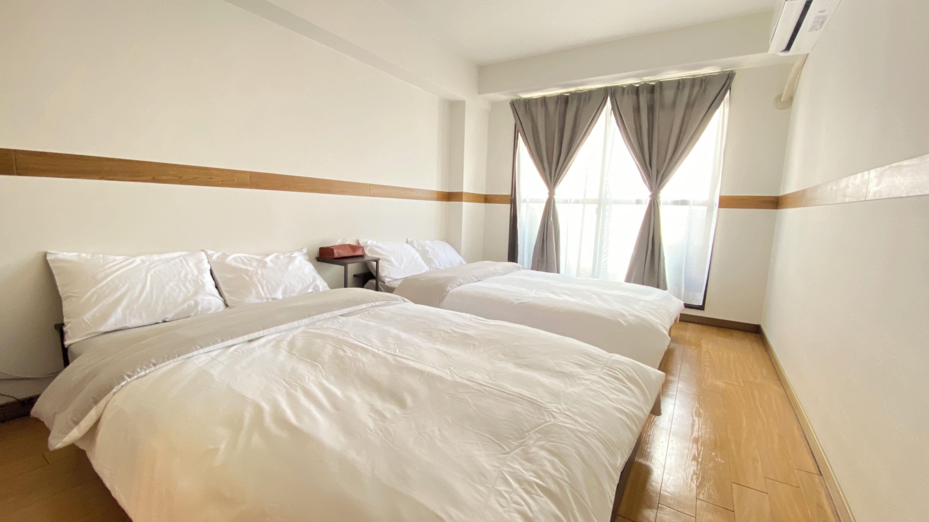 Een hotelkamer met twee bedden, een houten vloer en een raam met gordijnen.