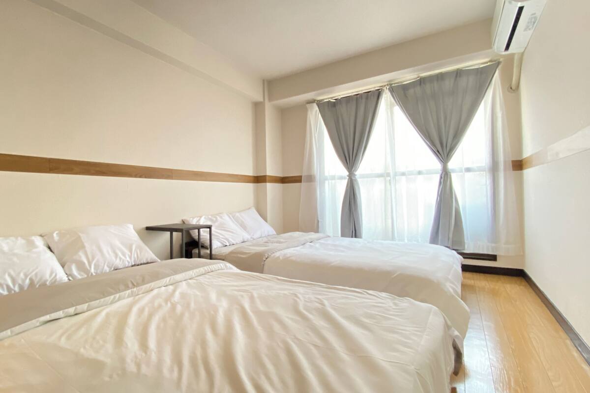 A hotel room with two beds, a small table, and a window with curtains.