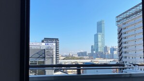 Une vue depuis une fenêtre donnant sur un paysage urbain avec des bâtiments modernes, dont un gratte-ciel imposant et un bâtiment portant l’enseigne « Toyoko Inn ».