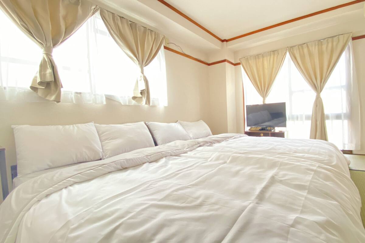 A hotel room with a large bed, a flat-screen TV, and curtains on the windows.
