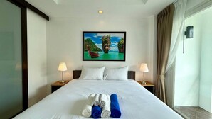 A hotel room with a large bed, two bedside tables with lamps, a painting of a tropical scene, and neatly folded towels on the bed.