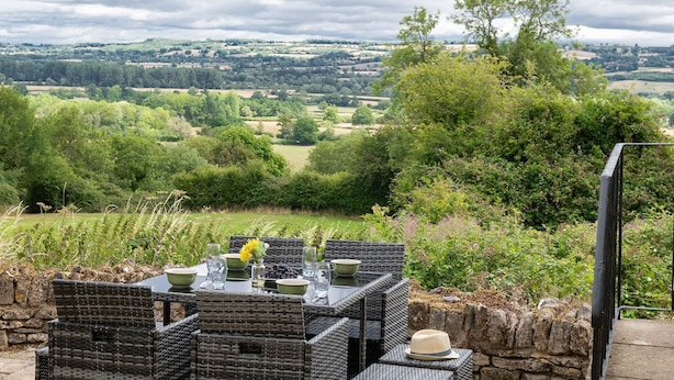 An outdoor dining area with wicker furniture and a table set for two, overlooking a scenic countryside view. - Murray's Cottage - sleeps 5 guests  in 3 bedrooms (Bourton-on-the-Water)