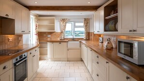 A kitchen with wooden countertops, white cabinets, a built-in oven, a microwave, and a window with curtains. - Murray's Cottage - sleeps 5 guests  in 3 bedrooms (Bourton-on-the-Water)