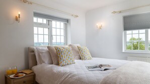 A bedroom with a large bed, two bedside lamps, a window with a view, and a nightstand with glasses and a book. - Murray's Cottage - sleeps 5 guests  in 3 bedrooms (Bourton-on-the-Water)