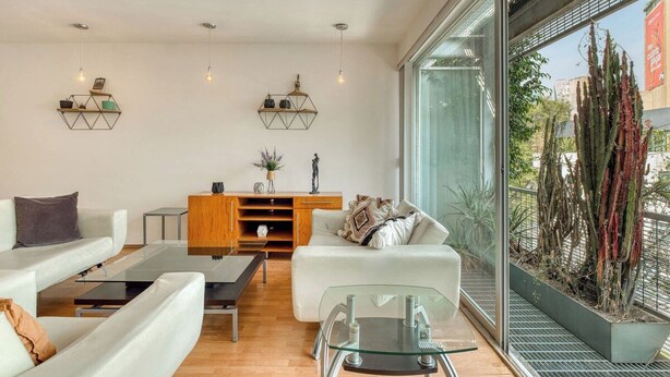 Een moderne woonkamer met een glazen salontafel, witte banken en een houten kast.