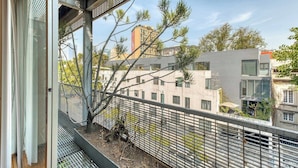 Een balkon met een metalen hekwerk, uitzicht op een gebouw en een boom.
