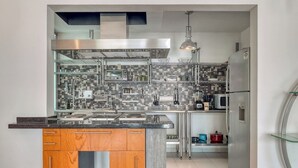 Een moderne keuken met een centraal eiland, roestvrijstalen apparatuur en een betegelde achterwand.