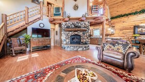 A spacious living room with a stone fireplace, wooden staircase, leather sofa, and a large TV.