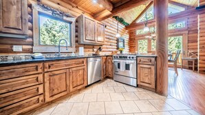 A log cabin kitchen with wooden cabinets, a stainless steel dishwasher, an oven, and a large window.