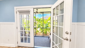 A room with a white door leading to a covered outdoor area with a view of greenery.